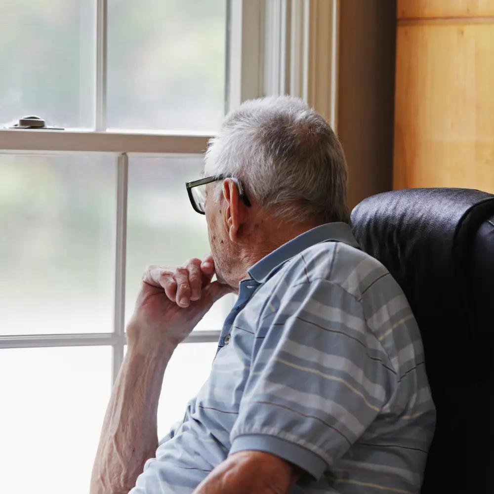 Adulto mayor sentado en casa mirando por la ventana, reflejando aislamiento social, una de las causas silenciosas de desnutrición en la tercera edad.